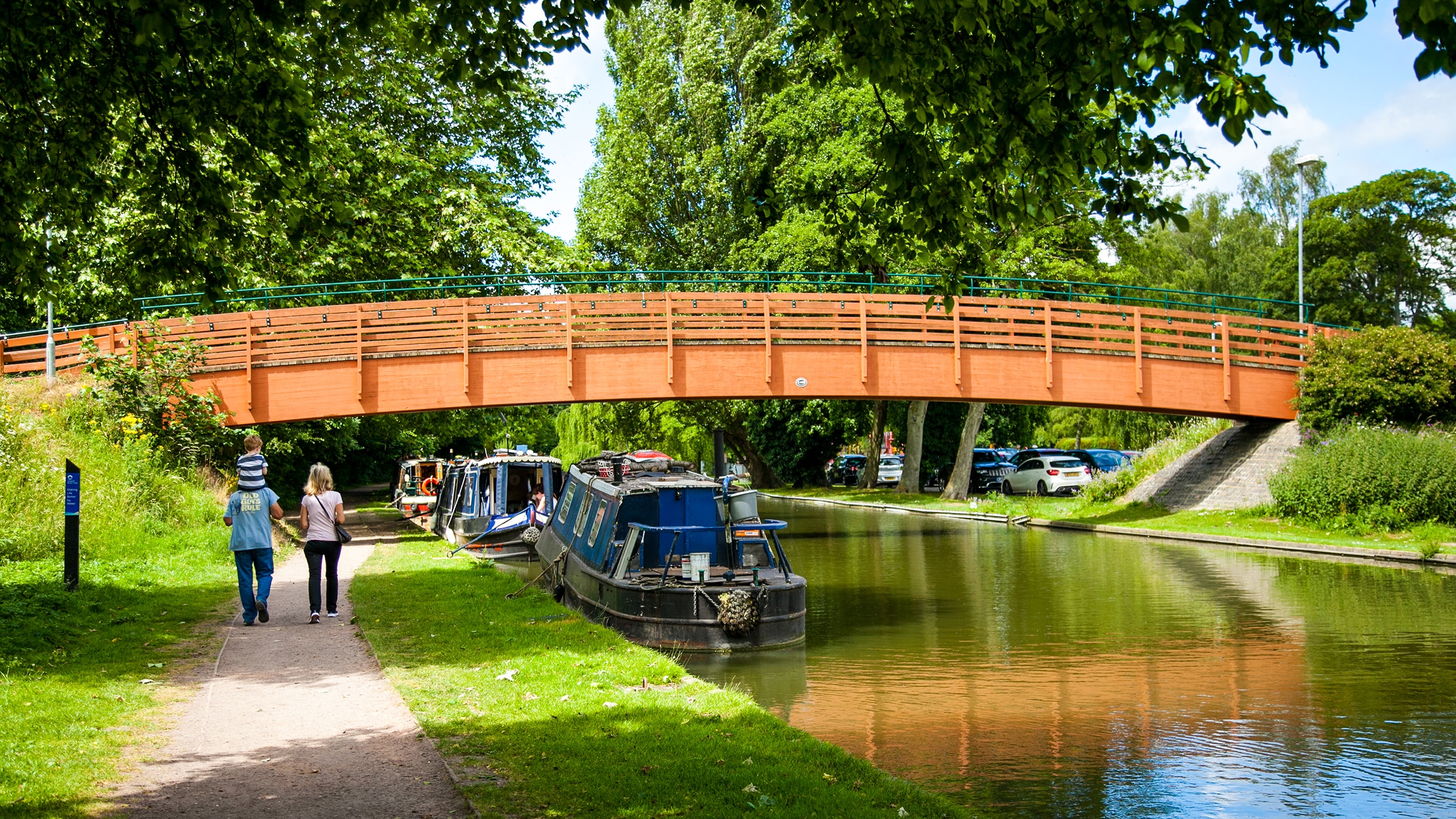 Canal & River Trust - Legacy Engagement & Development. A young family walking along a canal path by a newly develped footbridge on a warm and bright day.