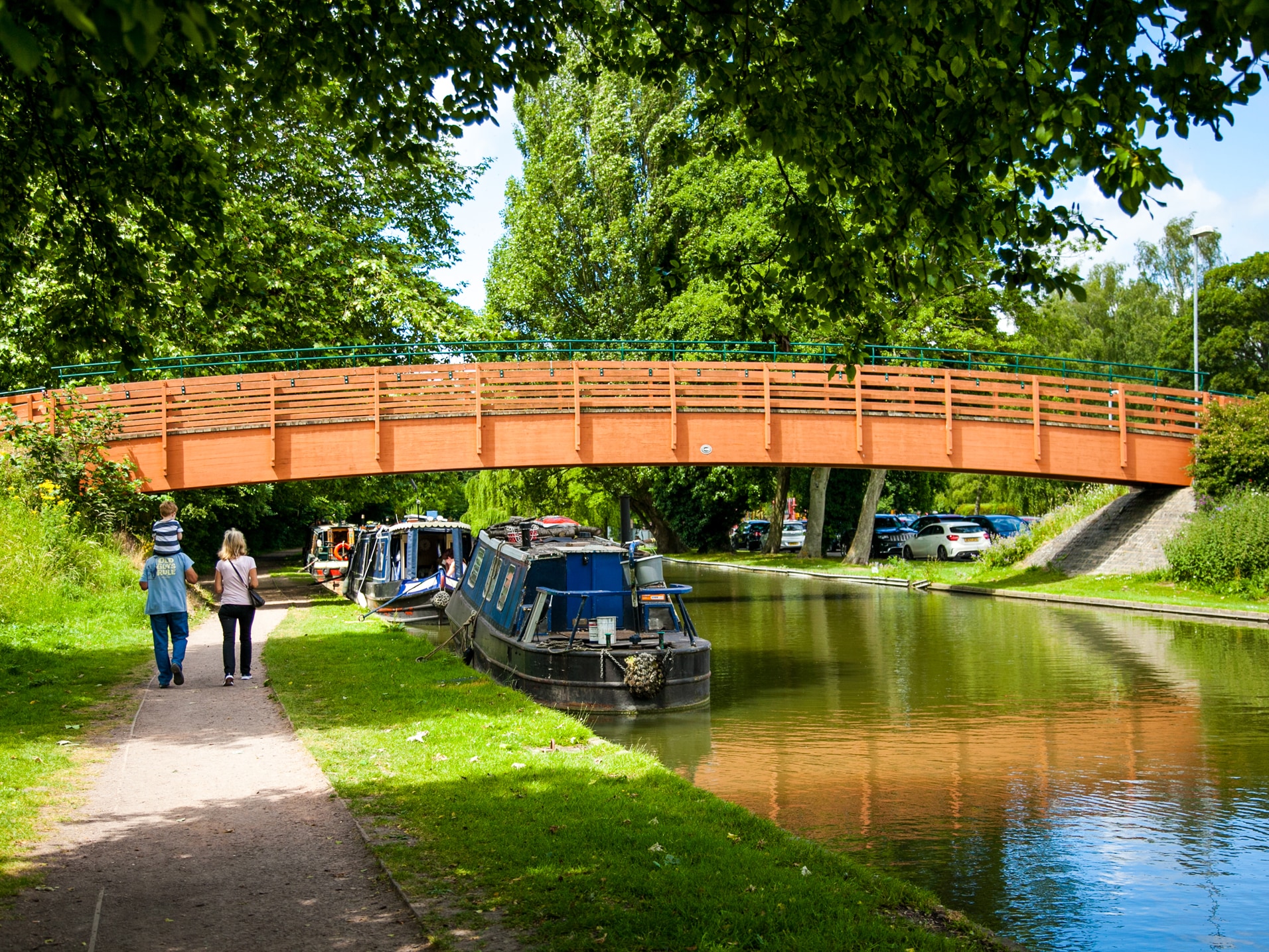 Canal & River Trust - Legacy Engagement & Development Canal & River Trust - Legacy Engagement & Development. A young family walking along a canal path by a newly develped footbridge on a warm and bright day.