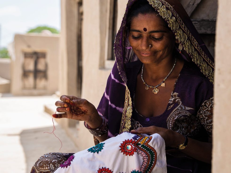 Y Care - Sharing the gift of Christmas. Woman in purple and gold traditional clothing, sat down while doing intricate needle work.